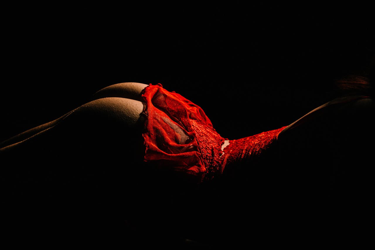 Striking studio shot of a woman posing in red lingerie against a dark background.
